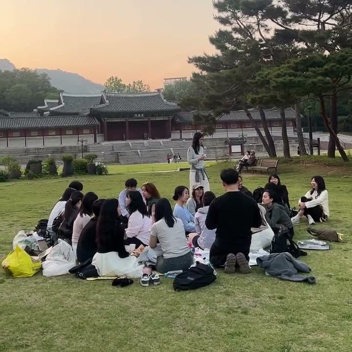 KND neighbors sitting in a circle on the grass at sunset outside the Seoul Museum of History